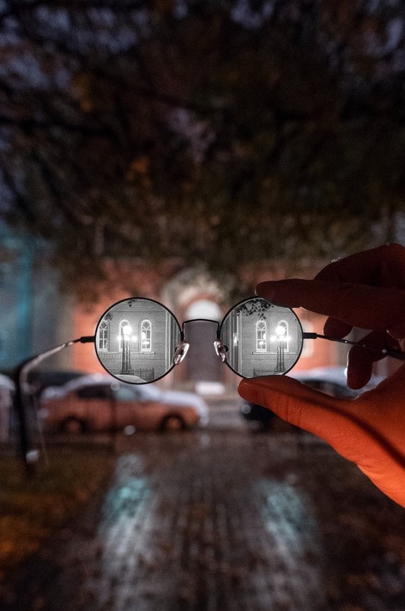 Photographie d'une personne tenant une paire de lunettes. À travers le verre, de la netteté et en dehors, du flou. Modification des verres pour avoir un contraste, de couleur noir et blanc.