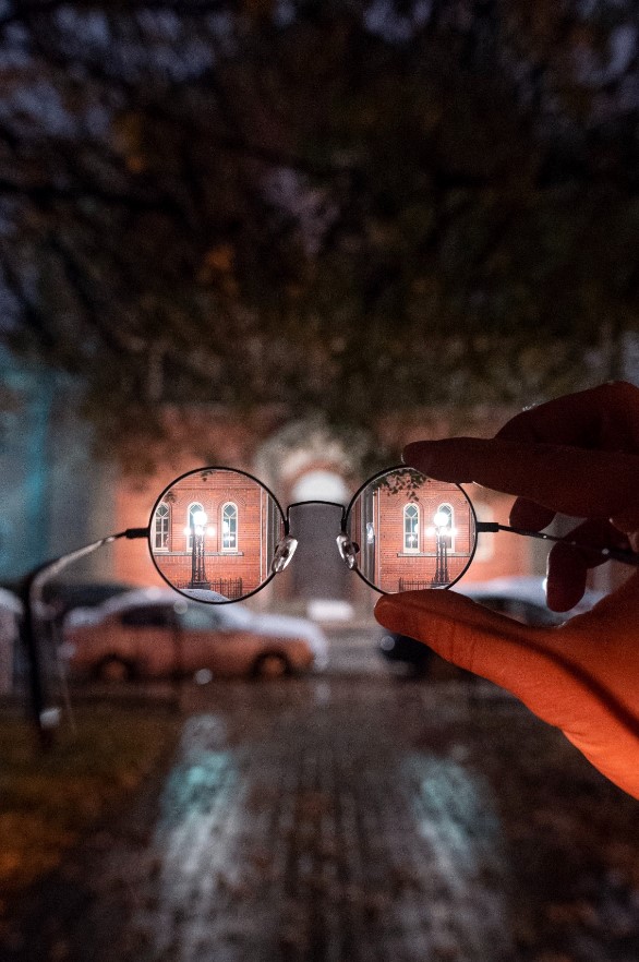 Photographie d'une personne tenant une paire de lunettes. À travers le verre, de la netteté et en dehors, du flou.